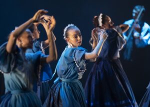 A Duna balladái – Táncok és imák a Duna mentén című előadás jelenete. Kék népviseletet viselő táncosnők lassú, emelkedett mozdulatokat végeznek a színpadon.