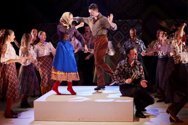 Apák előadás – férfi táncos ugró mozdulatban, körülötte népviseletbe öltözött csoport